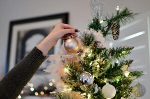 A hand decorates a Christmas tree with shiny ornaments, capturing the festive spirit.